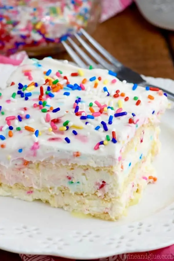 The No Bake Birthday Cake Lasagna has a pudding like texture middle speckled in between crackers with colors and on top with frosting and rainbow sprinkles. 