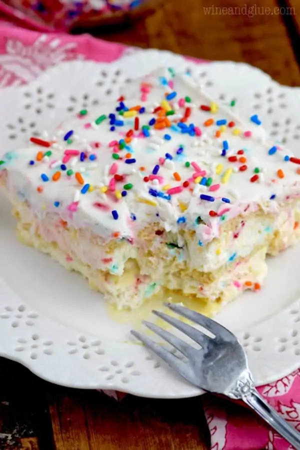 A slice of the No Bake Birthday Cake Lasagna is on a white plate with a small bite showing the rainbow speckles throughout the cake.