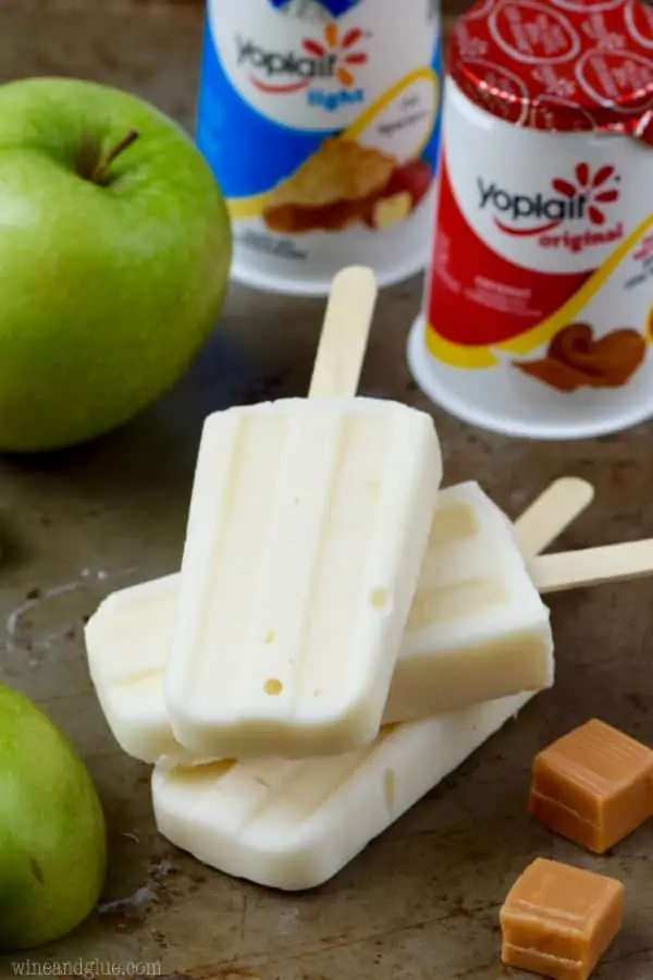 Three of the Lighter Caramel Apple Pipe Pops are stacked on top of each other and in front of the Yoplait yogurt. 