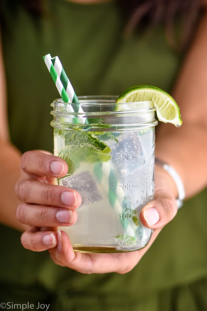 a woman holding a mason jar with a mojito in it