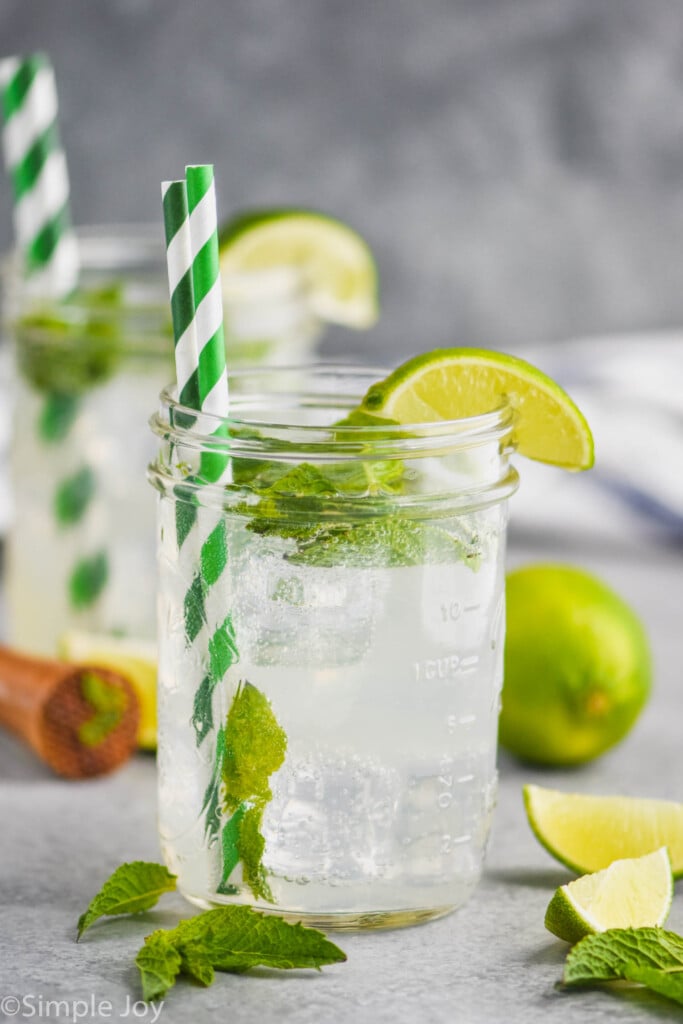 two mason jars with green striped straws and lime wedges holding skinny mojitos