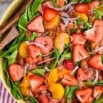 overhead of a strawberry salad with sliced strawberries, mandarin oranges, bacon, and red onions