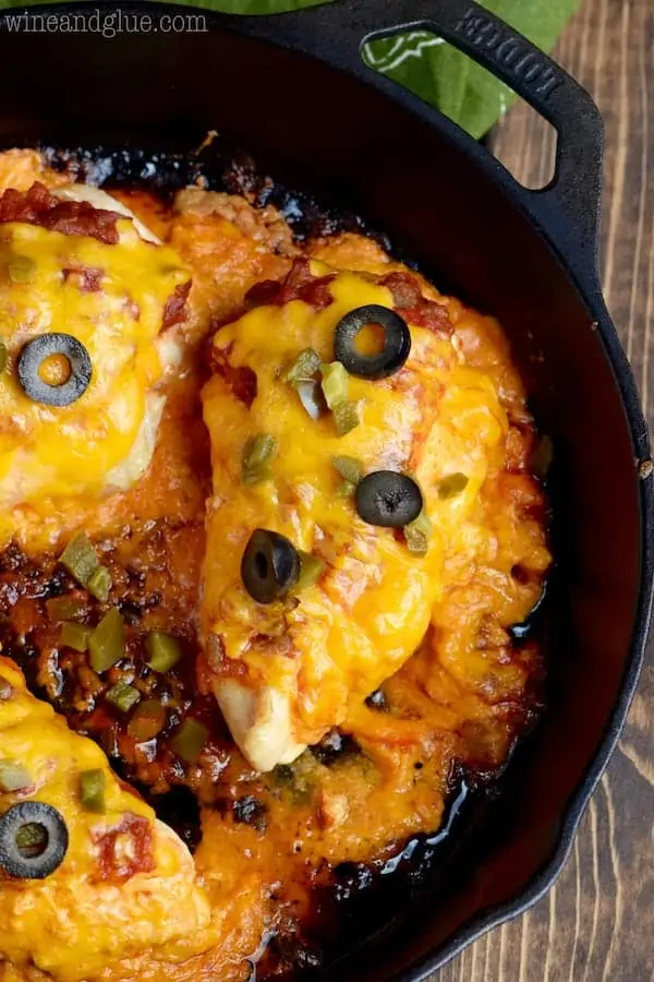 In a cast iron skillet, the Stuffed Taco Chicken is topped with melted cheese, olives, and minced jalapenos. 