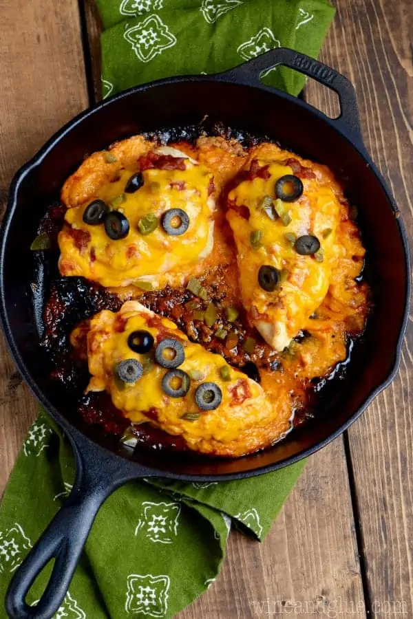 In a cast iron skillet, three Stuffed Taco Chickens are fully cooked with melted cheddar cheese, black olives, and minced jalapenos. 