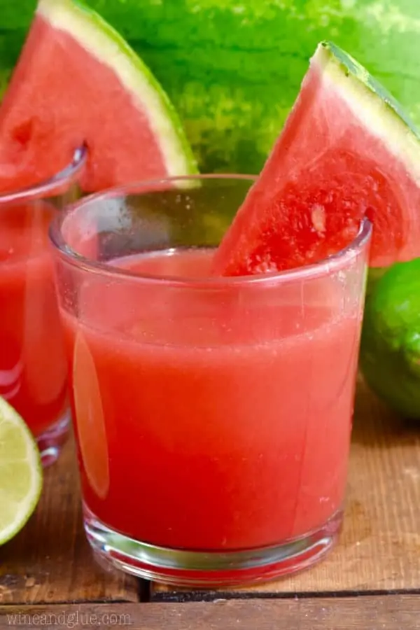 In a glass, the Watermelon Limeade has a red color and a slice of watermelon on the rim. 
