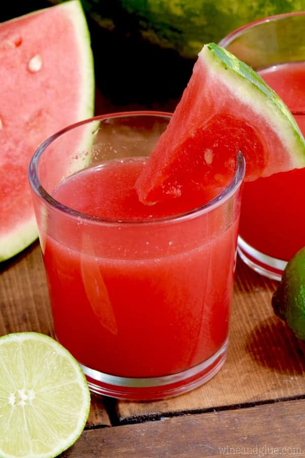 In a glass, the Watermelon Limeade has a red color and a slice of watermelon on the rim. 