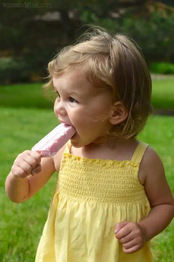 A little girl eating the yogurt popsicle. 