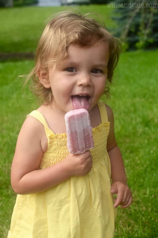 A little girl eating the yogurt popsicle. 