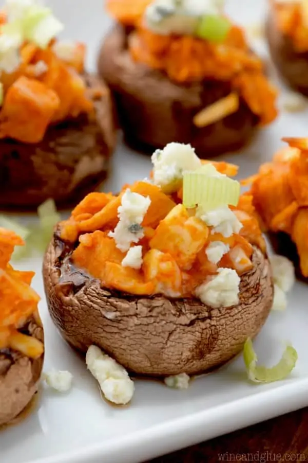 On a white plate, the mini Portobello Mushrooms are stuffed with buffalo chicken and topped with blue cheese and chives. 