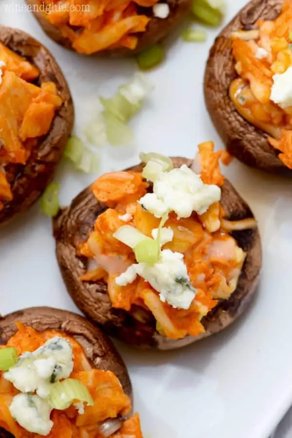 On a white plate, the mini Portobello Mushrooms are stuffed with buffalo chicken and topped with blue cheese and chives. 