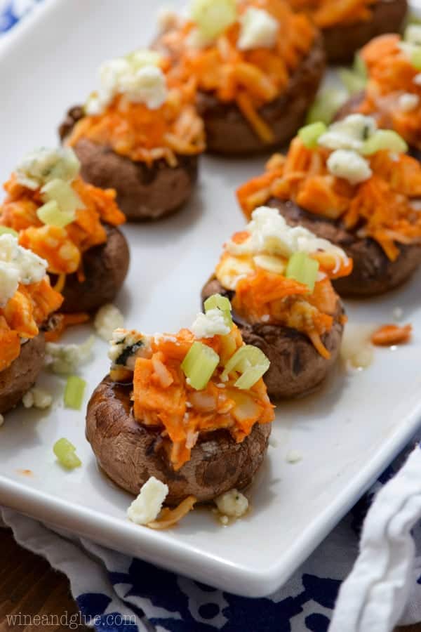 On a white plate, the mini Portobello Mushrooms are stuffed with buffalo chicken and topped with blue cheese and chives. 