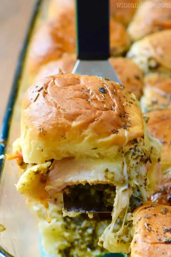 A spatula is lifting a an Italian Pesto Slider causing the melted cheese to stretch out. 