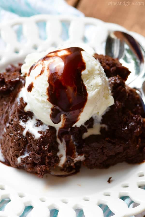 On a white plate, the Slow Cooker Hot Fudge Brownie has a scoop of vanilla ice cream and drizzled with chocolate syrup. 