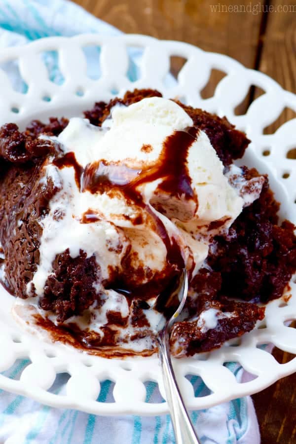 A spoon digging into the Slow Cooker Hot Fudge Brownies with a scoop of vanilla ice cream and a drizzle of fudge syrup. 