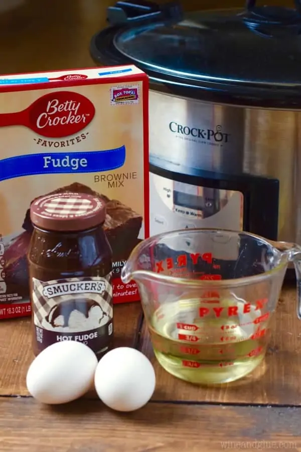 In front of the Crock Pot, the ingredients for the Slow Cooker Hot Fudge Brownies are two eggs, Smucker's Hot Fudge, Betty Crocker's Fudge, two eggs, and oil. 