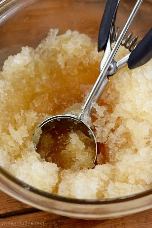 An ice cream scooper is scooping into the apple juice colored slush.  