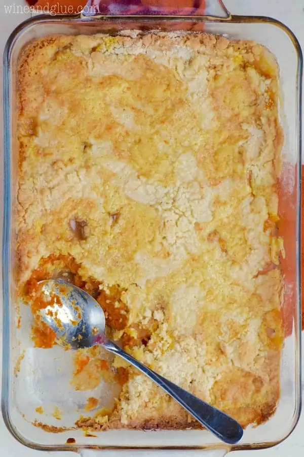 In a glass casserole dish, the Apple Pumpkin Dump Cake has a huge piece of it gone showing the moist pumpkin and apple inside. 