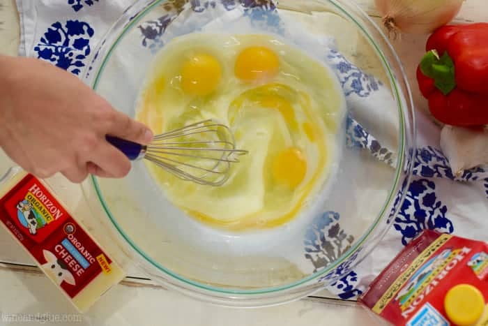 An overhead photo of a woman whisking four eggs in a glass bowl. 