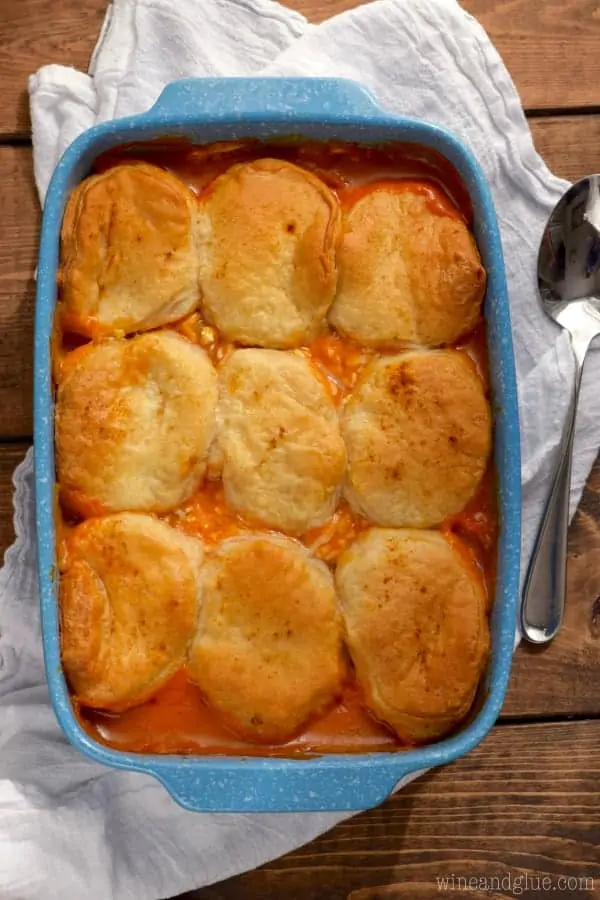In a blue casserole dish, the Buffalo Chicken Pot Pie has a bright red filling from the buffalo sauce and covered by golden brown biscuits. 