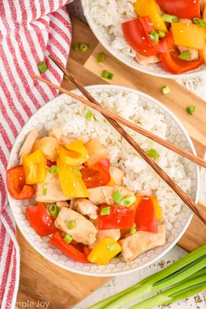 overhead view of a bowl of slow cooker sweet and sour chicken with rice, chopsticks laying over the top