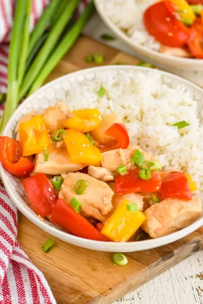 showing a shallow bowl holding sweet and sour chicken and rice, garnished with scallions