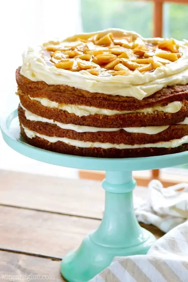 On a blue cake stand, the Naked Apple Spice Cake has raw edges and in between each cake there are some white fluffy frosting. 