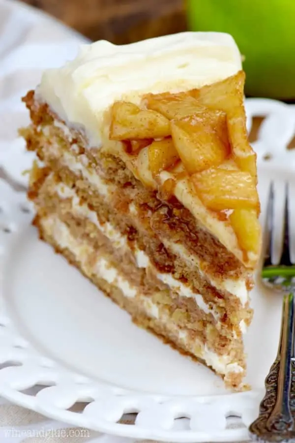 A slice of the Naked Apple Spice Cake is on a white plate showing the four distinct layers of the cake with fluffy frosting. 