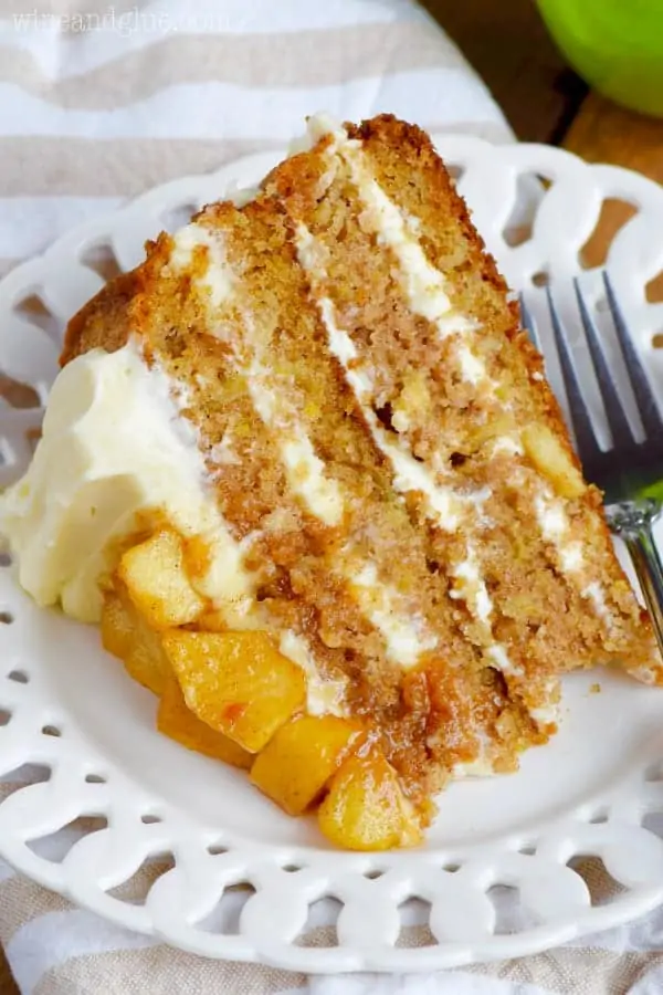 A slice of the Naked Apple Spice Cake is on a white plate showing the four distinct layers of the cake with fluffy frosting. 