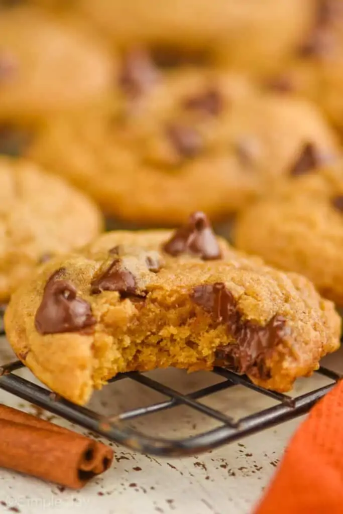 a pumpkin chocolate chip cookie on a cooling rack with a bite missing