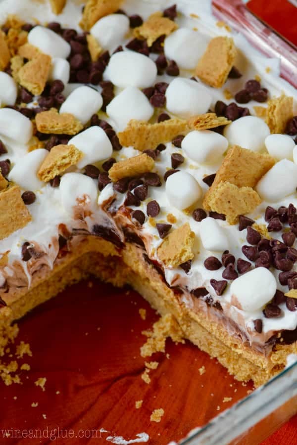 In a glass casserole dish, the Pumpkin S'mores Lush has a slice cut out showing the soft graham cracker layer. 