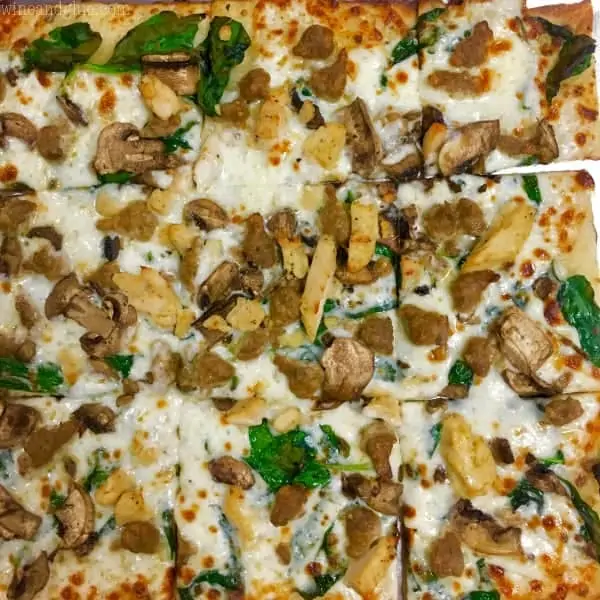 A close up photo of the Cali Alferdo Pizza that is topped with spinach, mushrooms, chicken, cheese, and with an Alfredo sauce. 