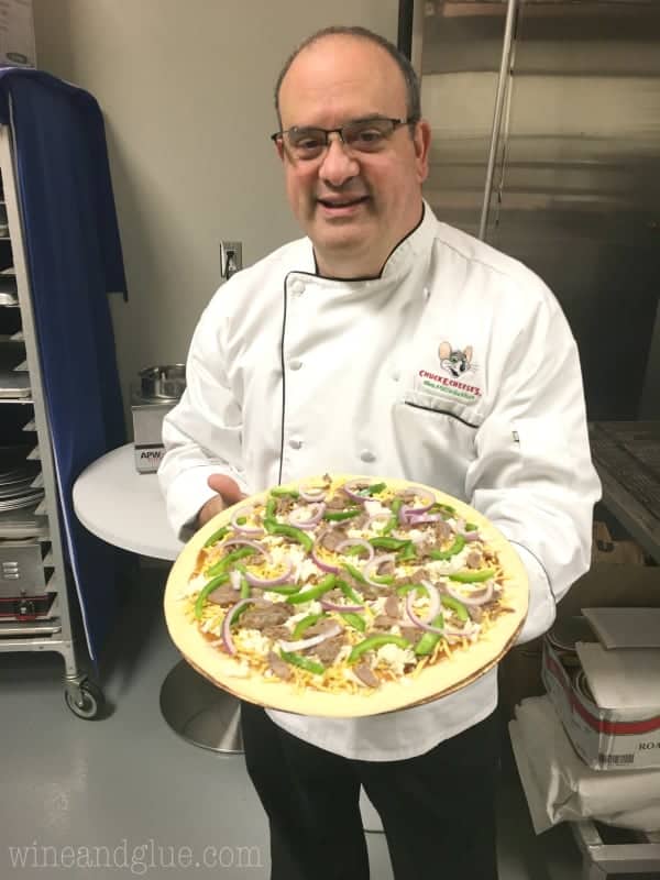 Chef Tony holding up an uncooked pizza that is topped with peppers, onions, and sausage. 
