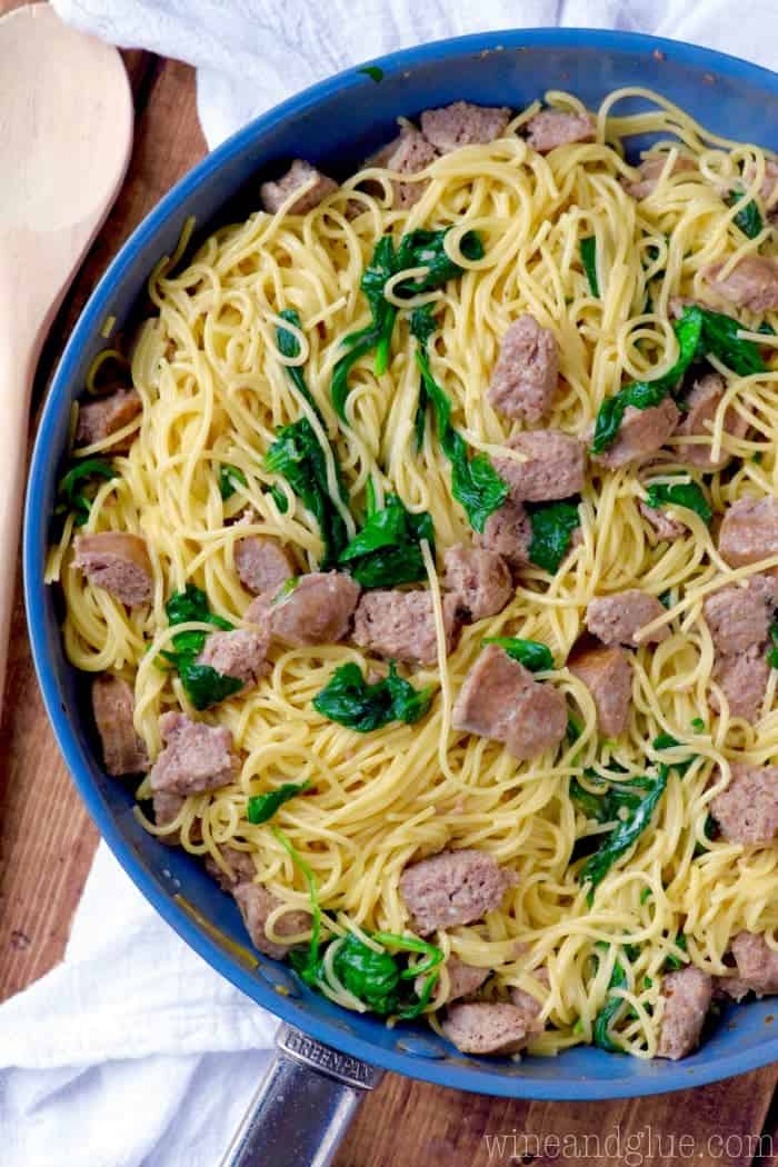 In a blue pot, the One Pot Creamy Spaghetti and Sausage is made with long spaghetti noodles, sausages, and spinach. 