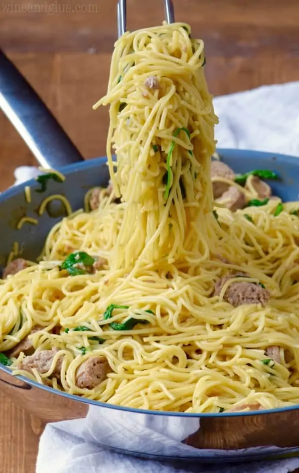 In a sauce pan, the One Pot Creamy Spaghetti and Sausage is picked up by a pair of tongs. 