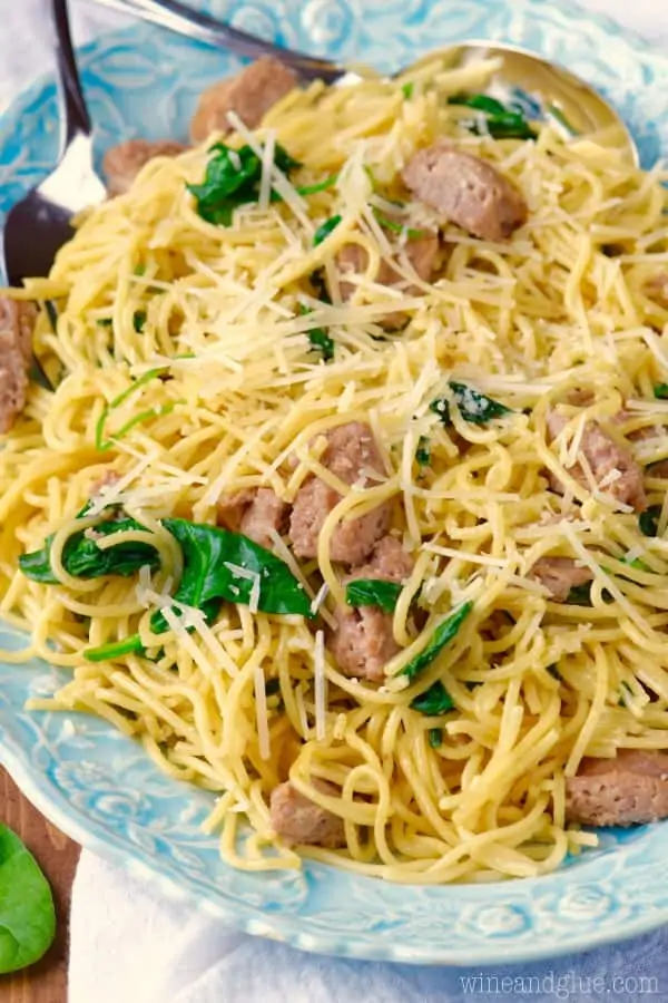 On a white plate, the One Pot Creamy Spaghetti Sausage has halved sausage slices and sautéed spinach topped with parmesan cheese. 