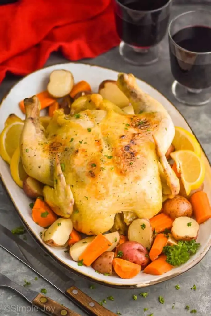 slow cooker whole chicken on a white platter surrounded by vegetables