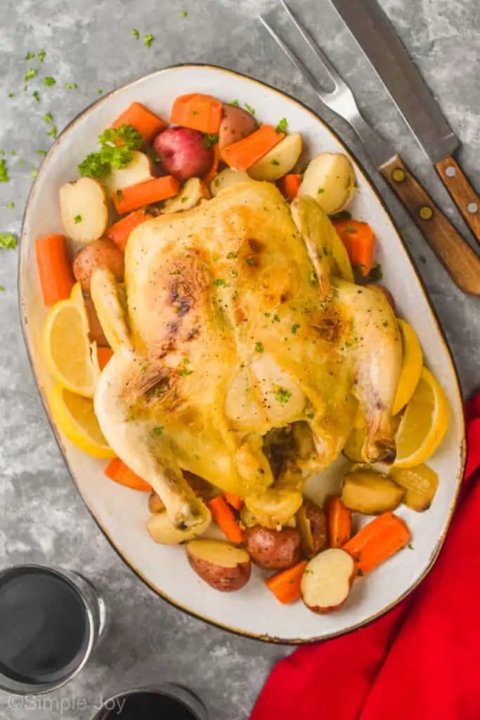 overhead view of a whole chicken on a platter surrounded by veggies and garnished with parsley