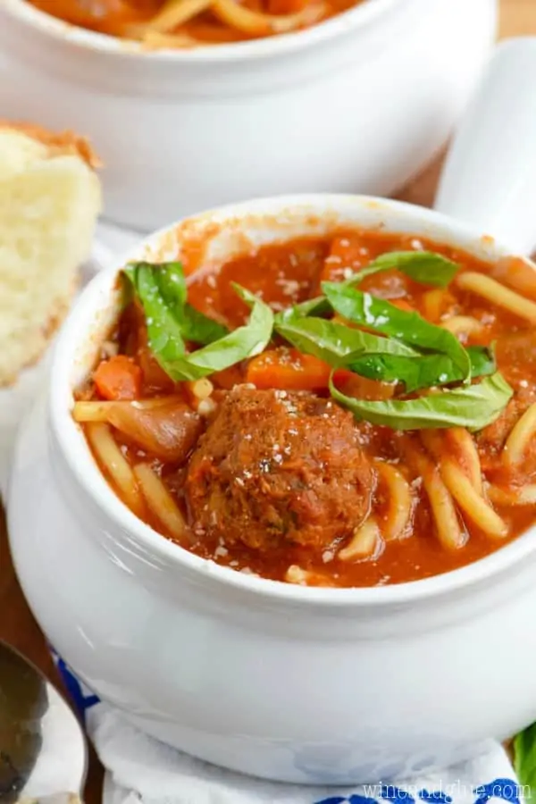 In a white bowl, the Slow Cooker Spaghetti and Meatball Soup is topped with sliced basil. 