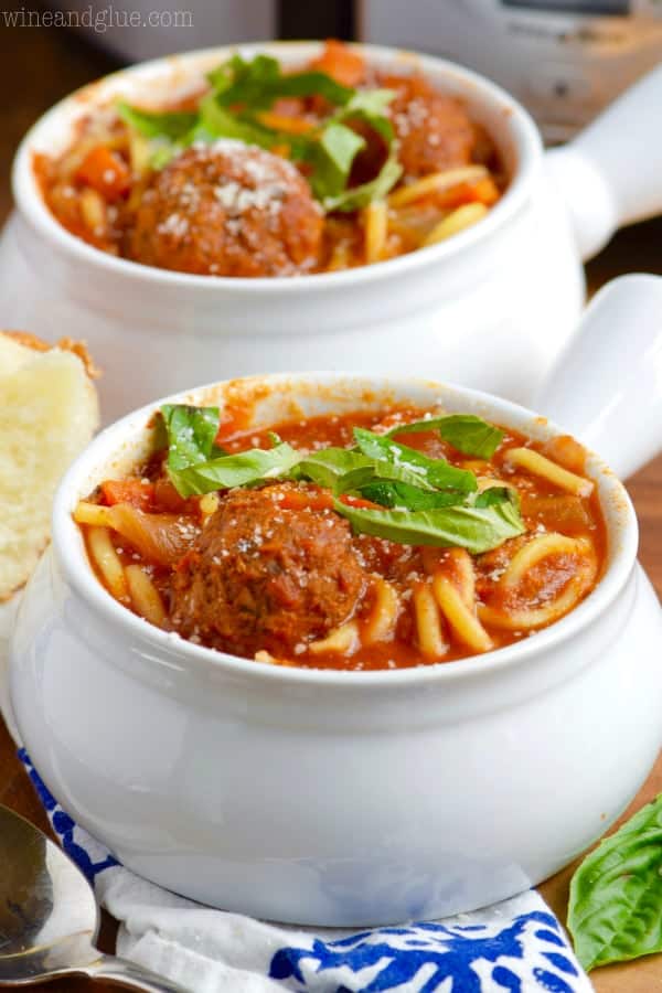In a white bowl, the Slow Cooker Spaghetti and Meatball Soup is topped with sliced basil. 