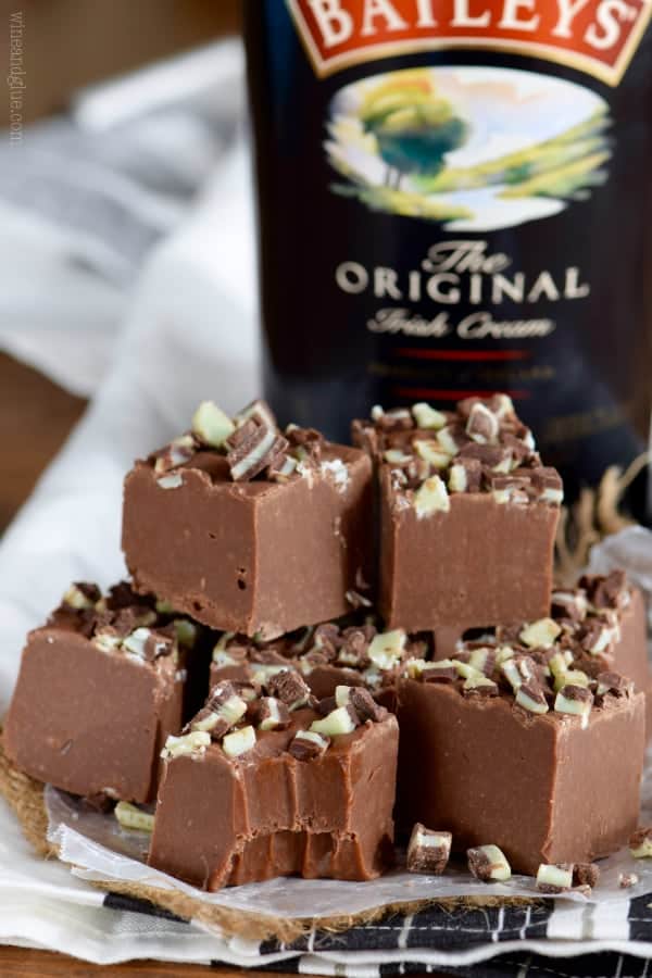 In front of a bottle of Bailey's, a stack of Bailey's Fudge topped with chopped up Andes chocolate