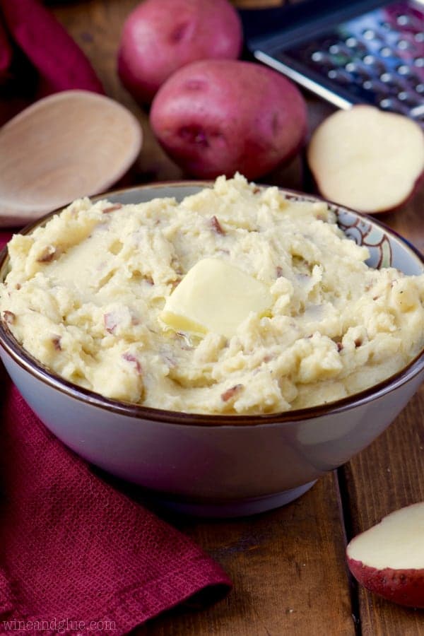 In a purple bowl, the Cheesy Crock Pot Mashed Potatoes is fluffy and creamy with a single slice of butter on top. 