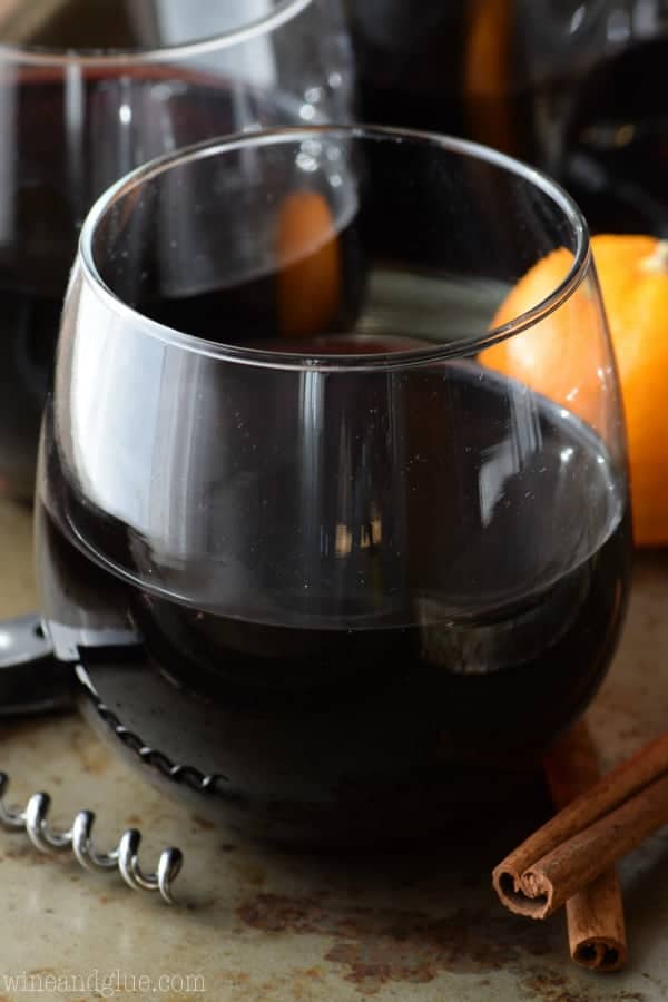 In a whine glass, the Cinnamon Sangria has an almost black color and surrounded by cinnamon sticks and oranges. 