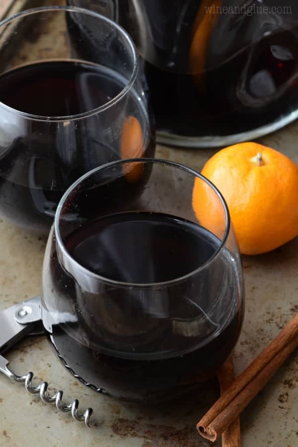 In a whine glass, the Cinnamon Sangria has an almost black color and surrounded by cinnamon sticks and oranges. 
