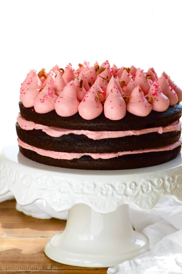 The Red Wine Chocolate has three layers has raw edges, pink frosting in the middle, and topped with cone like dollops of pink frosting, pink sprinkles, and shaved chocolate. 