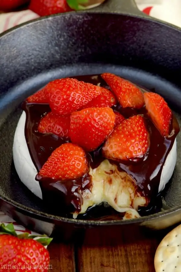 In a cast iron pan, the Chocolate Covered Strawberry Baked Brie has a little slice cut out showing the melted brie cheese. 