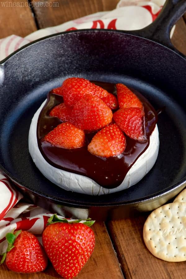 In a cast iron, the brie cheese is covered with melted chocolate and cut strawberries. 