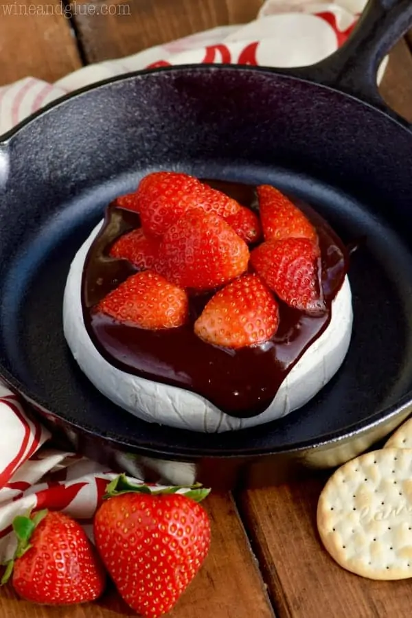In a cast iron, the brie cheese is covered with melted chocolate and cut strawberries. 