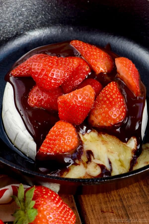 In a cast iron pan, the Chocolate Covered Strawberry Baked Brie has a little slice cut out showing the melted brie cheese. 
