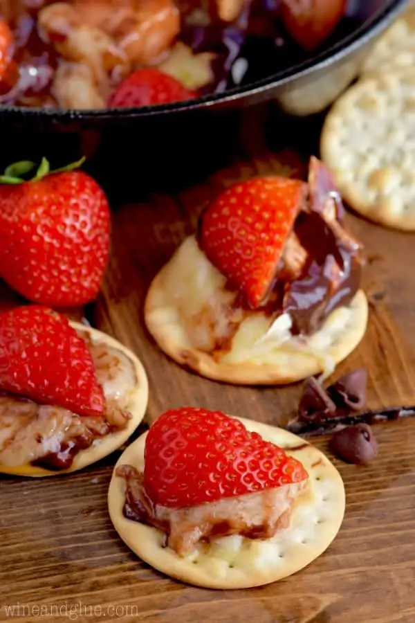A slice of the brie cheese and strawberry is covered in chocolate on a cracker. 