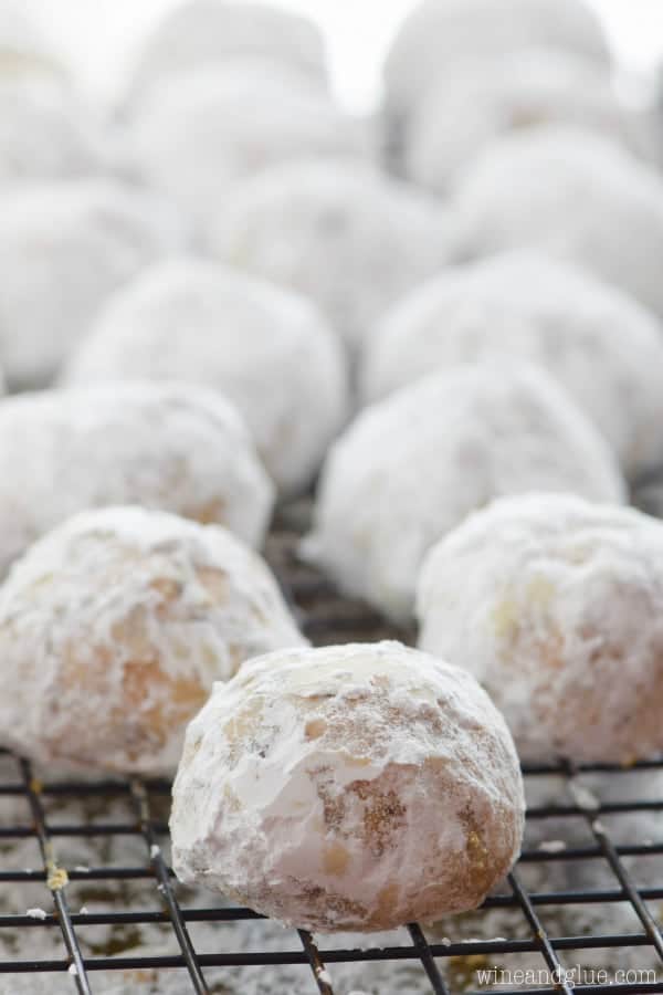 On a baking rack, there are lines of Peanut Butter Chocolate Chip Snowball Cookies tossed in powdered sugar. 